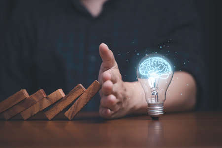 Hand protecting lightbulb with glowing virtual brain from falling wooden block , It is symbol of protect copyright and patent concept.の写真素材