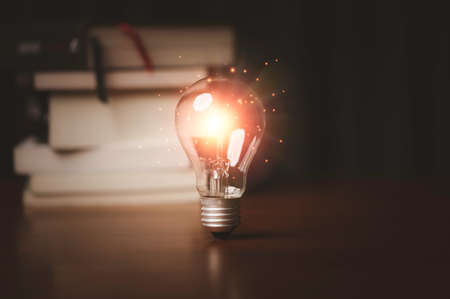 Orange light glowing from lightbulb infant of heap of books for study and learning can make creative thinking idea and knowledge to problem solving concept.の写真素材