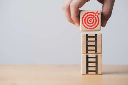 Hand holding red dartboard with arrow and ladder which print screen on wooden block for increasing...