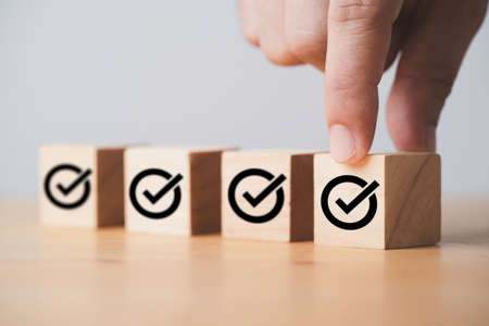 Hand putting correct sign which print screen on wooden cube block for approve project and ISO document concept.の写真素材