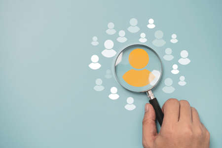 Hand holding magnifier glass with yellow person icon among white people icons for Customer focus group ,recruitment and human development concept.の写真素材