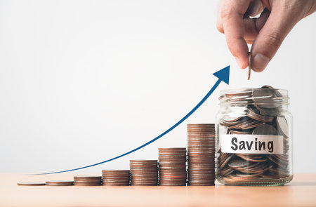 Hand putting coin to saving glass jar and increasing coins stacking with arrow for money save growth to investment , deposit banking and financial planing concept.の写真素材