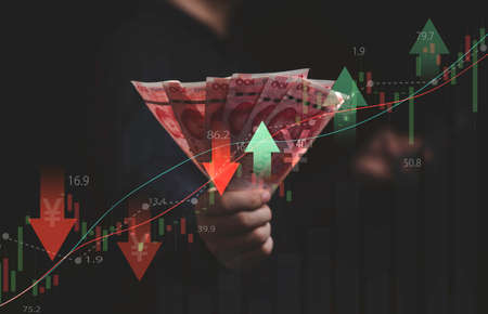 Businessman holding yuan banknote with stock market graph and up down arrow for inflation and interest rating increasing concept.の写真素材