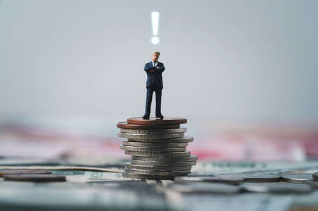 Businessman figure standing on coins stacking and thinking with exclamation or caution sign for financial planing and analysis before investment concept.の写真素材