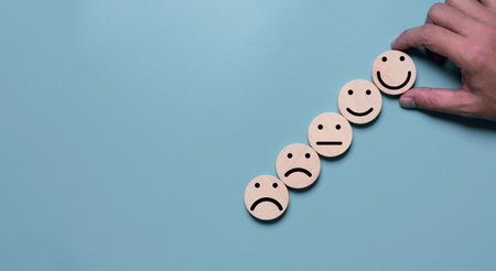 Hand holding smile face which print scree on round wooden among regular and sad emotion for excellent client evaluation after customer use product and service concept.の写真素材