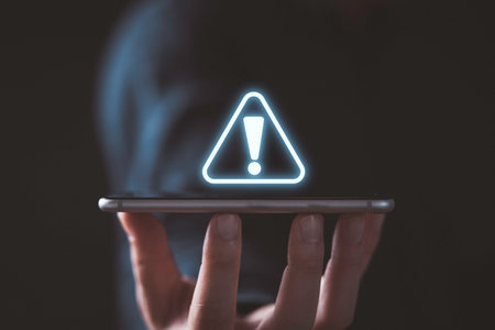 Businessman holding smartphone with triangle caution warning sign for notification error and maintenance concept.の写真素材