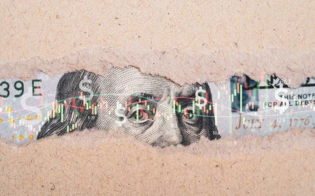 Closeup Benjamin Franklin face on USD banknote inside torn paper with stock market chart graph for currency exchange and global trade forex concept.の写真素材