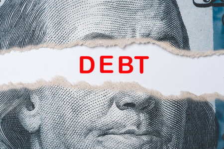 Benjamin Franklin face from USD dollar banknote behind of torn paper with debt wording for America's public debt is high and the debt ceiling needs to be raised concept.の写真素材