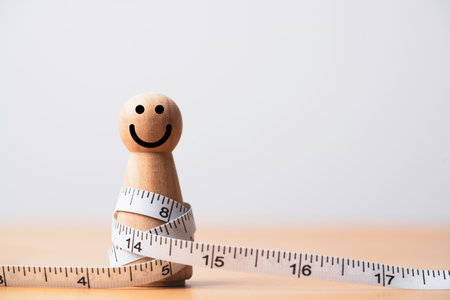 Fat wooden figure with measuring tape for happy diet and weight loss concept.の写真素材