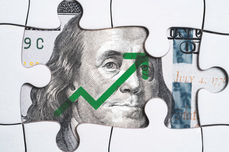 Closeup Benjamin Franklin face on USD banknote with increasing arrow behind jigsaw puzzle for currency exchange and global trade forex concept.の写真素材