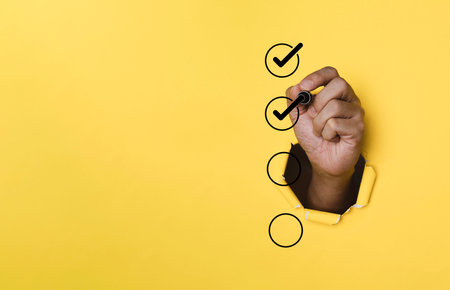 Hand use pen to tick correct sign mark in checkbox on punched yellow paper for quality document control checklist and business approve project concept.の写真素材