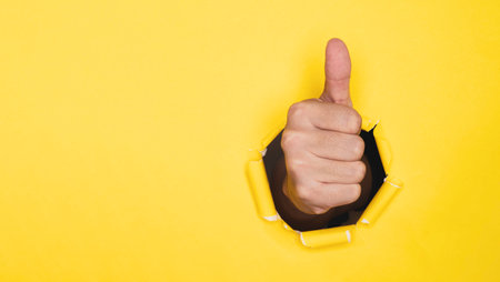 Businessman hand thumb up from yellow punched paper for client the best satisfaction evaluation survey after use product and service concept.の写真素材