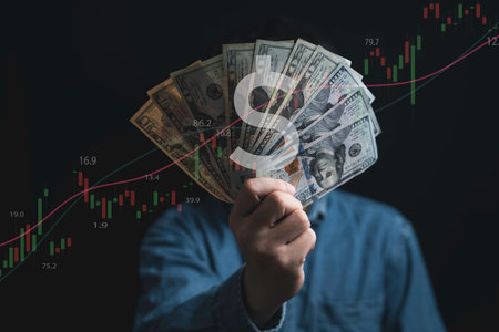 Hand holding USD dollar banknote with stock market chart and increasing arrow for dollar exchange ,...