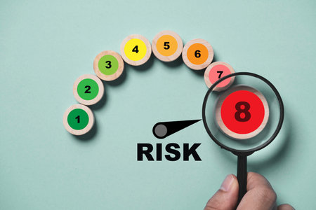 Hand holding magnifier glass with risk level indicator rating print screen wooden cube block since low to high on blue background for  focus risk Assess management of investment and working concept.の写真素材