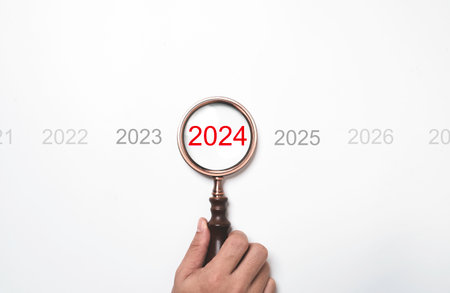 Hand holding magnifier glass with 2024 year for focus in new business of happy new year and merry...