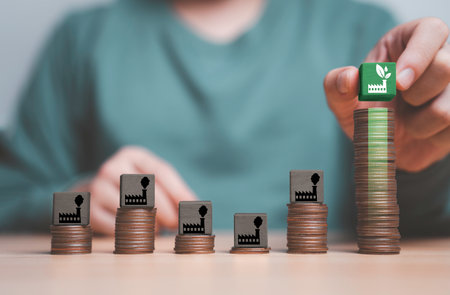 Businessman holding green factory icon on green block and stack on the top of highest coins for...