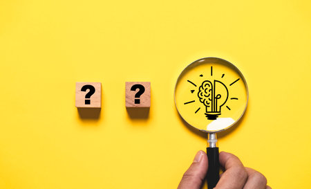 Hand holding magnifier glass with brain lightbulb lamp and question mark on yellow background for focus creative thinking idea to problem solving and patent innovation concept.の写真素材