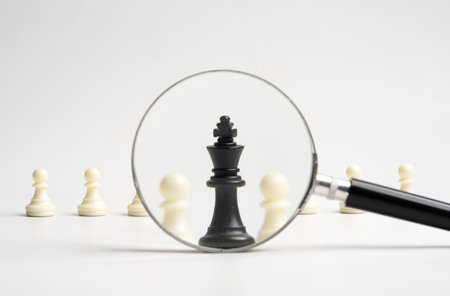 Black king chess standout with magnifier glass from white pawn chess for sign of leadership and management boss concept.の写真素材