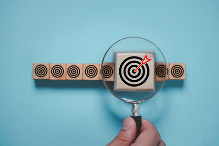 Hand holding magnifier glass to focus dartboard with arrow for business achievement objective goal and target concept.の写真素材