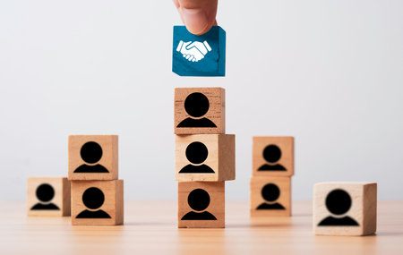 Hand putting Hand shaking on the top of human icon of wooden block cube for business deal and agreement concept.の写真素材