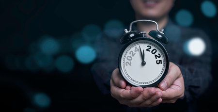 Businessman holding 2024 and 2025 on black alarm clock with copy space  for preparation of Merry Christmas and Happy new year concept.の写真素材