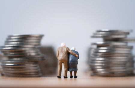 Miniature figure of Couple Senior Pensioners standing between coins stacking  for wealth financial planning ,money saving and life insurance of retirement concept.の写真素材