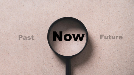 Now wording inside of Magnifier glass on brown background for focus current situation , positive thinking mindset concept.の写真素材