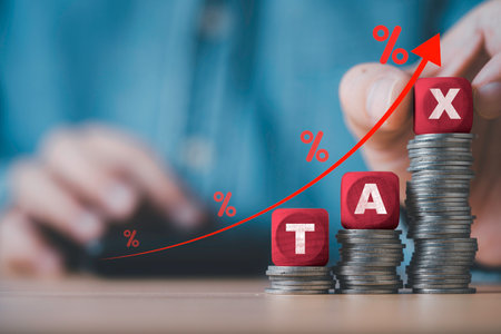 Businessman putting red tax wording on the top of coins stacking for government increasing tax expense to all person concept.の写真素材