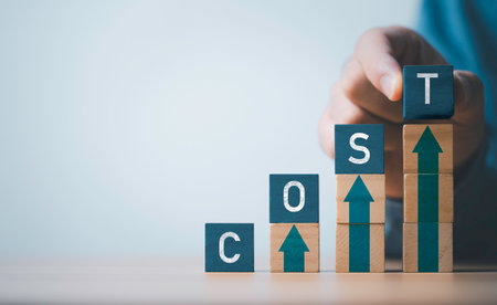 Businessman stacking of cost wording on the top of wooden block cube with up arrow for cost of product and manufacturing increase concept.の写真素材