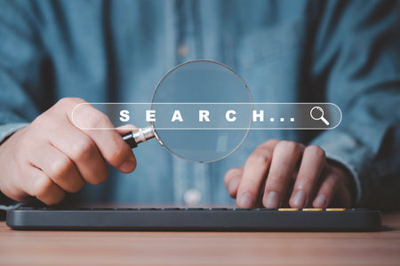 Businessman hold magnifier glass and use computer keyboard for search engine optimization or SEO ,...