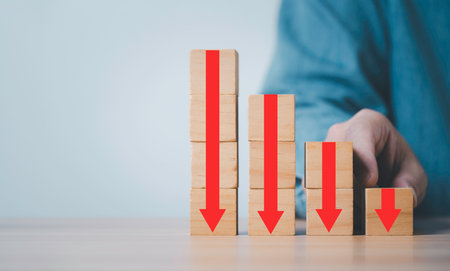 Businessman holding red down arrow which print screen on wooden block cube and copy space for cost profit economy and benefit decreasing concept.の写真素材