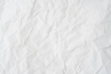 Close-up of crumpled white paper, showcasing its texture and subtle shadows. The irregularities create a sense of depth and complexity, perfect for artistic backgrounds or minimalist designs conceptの写真素材