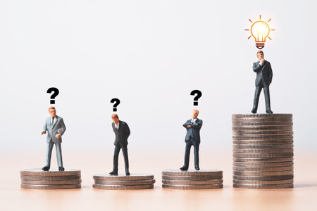 Businessmen miniature figure standing on  the top of coins stacking with glowing lightbulb and question mark for creative thinking idea and problem solving can make more profit of investment concept.の写真素材