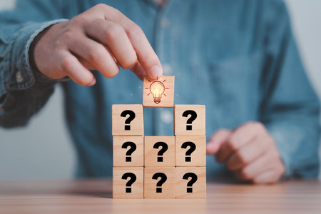Hand putting wooden cube block stacking which print screen glowing light bulb and question mark for Creative thinking idea and problem solving concept.の写真素材
