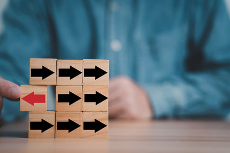 Wooden blocks with black arrows pointing right and one red arrow pointing left, symbolizing leadership, innovation, change management thinking outside the box in business strategy  and disruption concept.の写真素材
