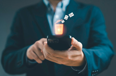 Businessman using smartphone with digital trash bin icon and deleting files representing data management cybersecurity privacy storage cleanup document removal and information security conceptの写真素材