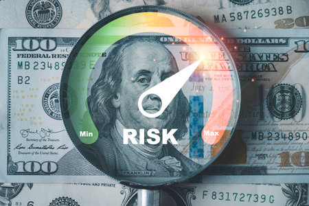 Financial risk concept showing a magnifying glass over US dollar bills with a risk gauge pointing to maximum level symbolizing investment danger finance uncertainty and market volatilityの写真素材