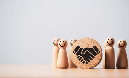 Wooden figures with smiling faces and handshake symbol showing teamwork trust cooperation success partnership communication and positive relationship concept in business and organizationの写真素材