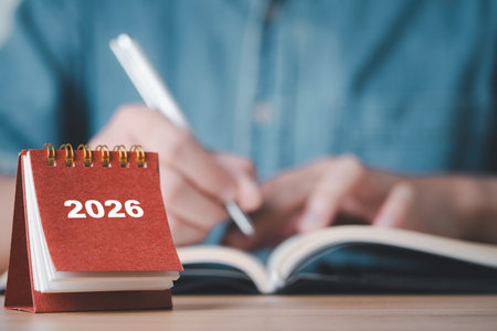 Showing a 2026 desk calendar with a person writing in a notebook representing planning organization future goals time management and preparation for the upcoming year in business and personal lifeの写真素材