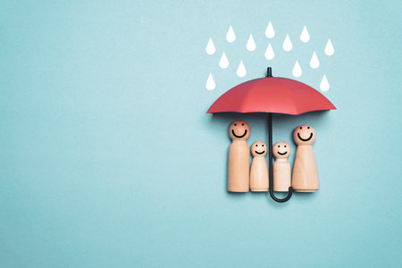 Wooden family figures standing under a protective umbrella with falling raindrops symbolize insurance safety security family care risk protection and financial planning for business and creative use.の写真素材