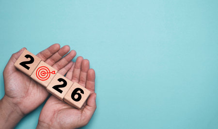 Hands holding wooden blocks forming 2026 with a target icon that represents future goals planning strategy business vision motivation and success on a simple and clean minimalist backgroundの写真素材