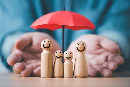 Wooden family figures under a red umbrella symbolizing protection insurance safety support and care with hands surrounding them to represent security risk management and family well beingの写真素材