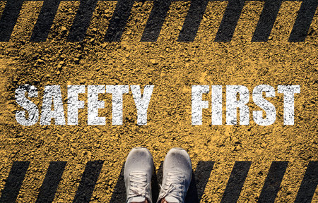 A top-down view of shoes standing on a textured road with bold Safety First text and caution stripes...