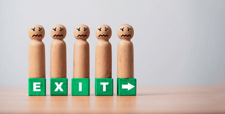 Wooden people figures with worried faces standing on exit blocks symbolize employee layoff job loss workforce reduction economic downturn business crisis and uncertainty on clean minimal background.の写真素材