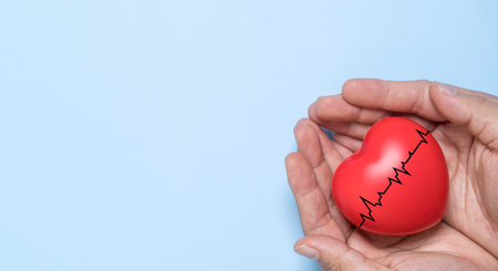 Hands holding red heart with heartbeat line on blue background represent heart health protection of...