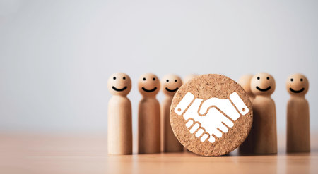 Handshake agreement icon in front of figures symbolizing partnership, teamwork and business collaboration. Trust building, customer relationship and corporate cooperation concept with copy space.の写真素材
