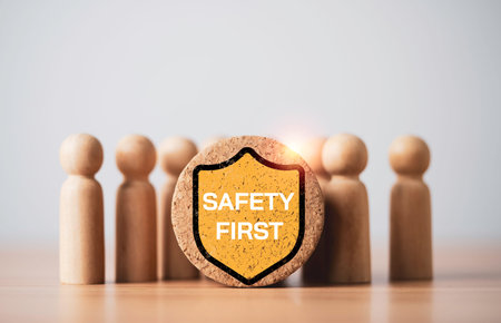 Safety first shield icon in front of wooden figures symbolizing workplace safety, employee protection and risk management. Corporate compliance and occupational health concept with copy space.の写真素材