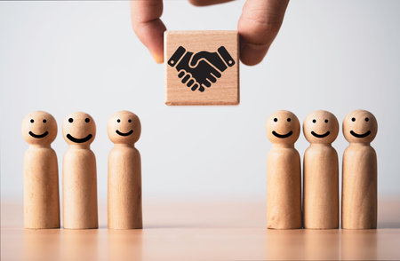 Business partnership and customer relationship concept with wooden figures and handshake icon. Trust building, teamwork collaboration and agreement strategy theme symbolizing cooperation and loyalty.の写真素材