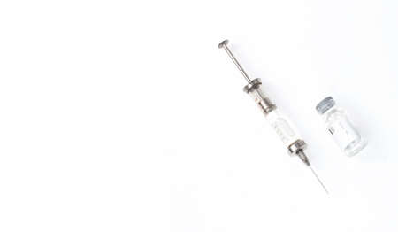 a syringe filled with medicine, next to a jar of medicines on an isolated white backgroundの写真素材