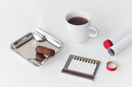 Ashtray with a smoldering cigar a cup of coffee and an open box of matches, on an isolated white backgroundの写真素材